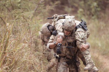 Kamuflaj üniformalı askerler silah taşıyorlar. Tropikal orman bölgesinde keşif görevleri var. Yaralıların vurulmasına yardım etmek için.