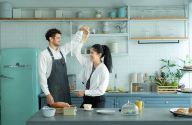 Bir koca karısıyla yemek pişirirken önlük giyer. Yemek pişirmek için mutfağa girmeden önce mutlu bir şekilde dans ediyordu..