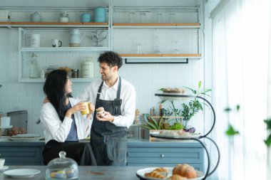 Bir koca karısıyla yemek pişirirken önlük giyer. İkili kahve yudumlamak ve tamamlanmış ekmeği tatmak için mola verdi..