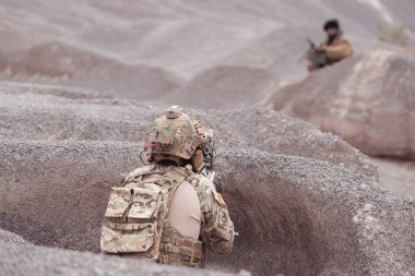 Bir Taliban askeri elinde makineli tüfekle çöl dağlarındaki savaş meydanında müttefik askerlere teslim olur.