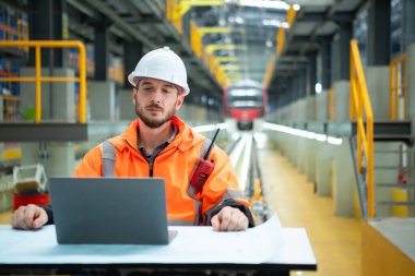 Skytrain tamir istasyonunda masada oturan genç erkek teknisyenin portresi dizüstü bilgisayardaki elektrik tren tamirinin detaylarını kontrol et.