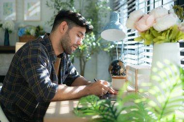 Evde bilgisayarla çalışan yakışıklı genç adam, ev konseptiyle çalışıyor..
