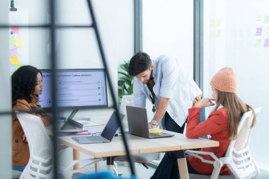 Modern parlak ofis içi beyin fırtınasında toplanan çok ırklı girişim ekibi dizüstü bilgisayar ve tablet bilgisayar üzerinde çalışıyor