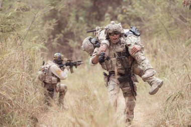 Kamuflaj üniformalı askerler silah taşıyorlar. Tropikal orman bölgesinde keşif görevleri var. Yaralıların vurulmasına yardım etmek için.