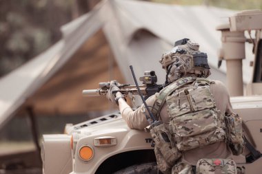 Kamuflaj üniformalı askerler, askeri haberleşme aracının yan tarafında saklanarak silahlarını ateşe hazır tutuyorlar.