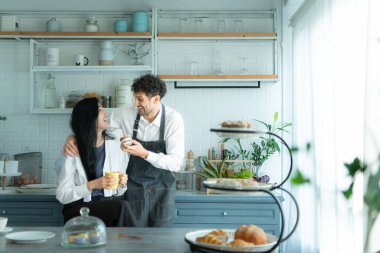 Bir koca karısıyla yemek pişirirken önlük giyer. İkili kahve yudumlamak ve tamamlanmış ekmeği tatmak için mola verdi..