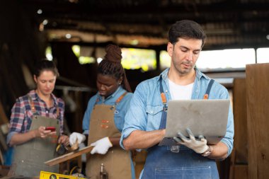 Portrait of carpenter male worker standing with laptop in workshop clipart