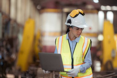 Demiryolu teknisyeninin portresi. Güvenlik yeleği ve miğferi var. Tren tamir istasyonunun planlarıyla çalışıyor.