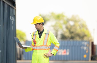 İthalat ve ihracat sektöründeki işçiler dizüstü bilgisayar tutuyorlar ve konteynırın ön tarafında konteynırın kargosunu incelemek için duruyorlar..