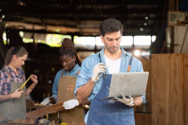 Portrait of carpenter male worker standing with laptop in workshop clipart