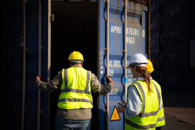 Boş bir konteynır deposunda çalışan bir grup işçi, eski konteynırın durumu, kullanım için bakım gerekip gerekmediğini belirlemek için değerlendiriliyor..