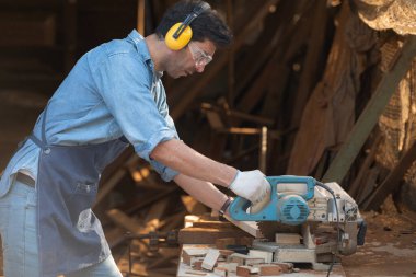 Bir ahşap atölyesinde testereyle çalışan bir zanaatkarın portresi.