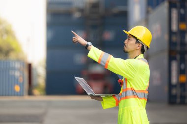 İthalat ve ihracat sektöründeki işçiler dizüstü bilgisayar tutuyorlar ve konteynırın ön tarafında konteynırın kargosunu incelemek için duruyorlar..