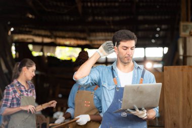 Portrait of carpenter male worker standing with laptop in workshop clipart