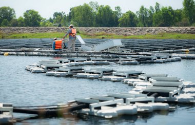 Her iki teknisyen de güneş enerjisi tarafından yüzen bir güneş enerjisi sisteminde üretilen elektrik nakil terminallerini değerlendiriyor ve onarıyor..