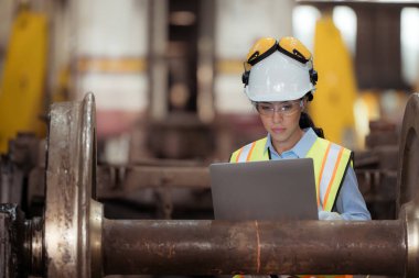 Üniformalı ve miğferli demiryolu teknisyeni tren atölyesindeki lokomotiflerden çıkarılan tren tekerleklerini inceleyin..