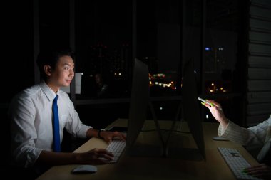 Her iki Asyalı genç borsacı uluslararası borsa simsarları gece ofisindeki masaüstünde birlikte çalışıyorlar. Uluslararası finans şirketi konsepti.