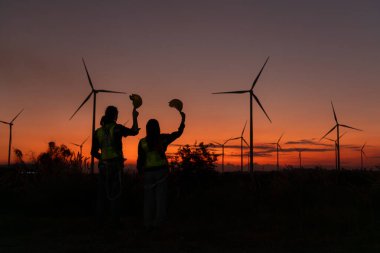 Engineers working on wind turbines farm at sunset, Wind turbines are alternative energy source. clipart