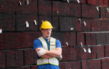 Portrait of a construction worker standing with arms crossed in front of steels material wall clipart