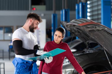 Bir oto tamirhanesinde profesyonel bir tamirci kadın müşteriye araba tamiratının maliyeti hakkında bilgi verir ve ödeme toplar..