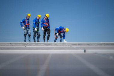 Arka planda mavi gökyüzü olan güneş panelleri üzerinde duran bir grup mühendis.