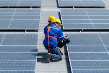 Her iki teknisyen de güneş enerjisini fabrikalarda kullanılmak üzere elektrik enerjisine çevirmek için deponun çatısına güneş panelleri kuruyor..