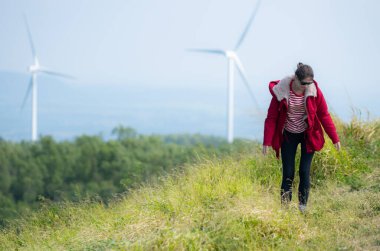 Yel değirmenlerinin arka planında, kırmızı ceketli genç bir kadın kış tatilinin tadını çıkarıyor..