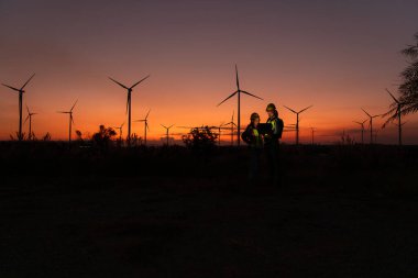 Engineers working on wind turbines farm at sunset, Wind turbines are alternative energy source. clipart