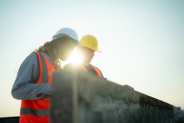İnşaat alanında çalışan erkek ve kadın mühendisler binanın duvarları ve balkonlarındaki çimento alçısını inceliyorlar..