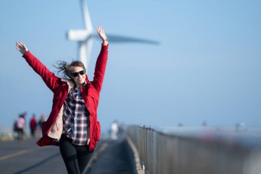 Yel değirmenlerinin arka planında, kırmızı ceketli genç bir kadın kış tatilinin tadını çıkarıyor..