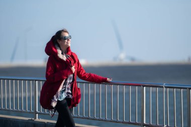 Yel değirmenlerinin arka planında, kırmızı ceketli genç bir kadın kış tatilinin tadını çıkarıyor..