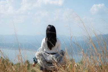 Mavi ceketli ve şapkalı Asyalı kadının dağın tepesinde duruşu.