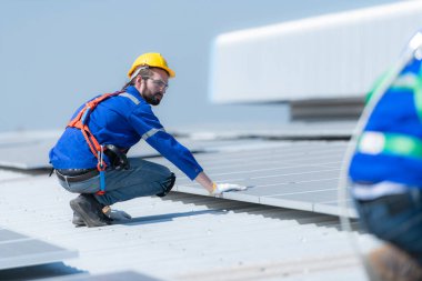 Her iki teknisyen de güneş enerjisini fabrikalarda kullanılmak üzere elektrik enerjisine çevirmek için deponun çatısına güneş panelleri kuruyor..