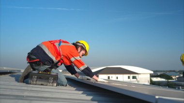 Her iki teknisyen de güneş enerjisini fabrikalarda kullanılmak üzere elektrik enerjisine çevirmek için deponun çatısına güneş panelleri kuruyor..