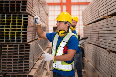 Depoda kasklı ve kasklı işçiler depodaki çeliği saymak ve teftiş etmek için bekliyor..