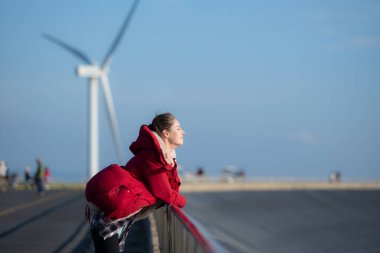 Yel değirmenlerinin arka planında, kırmızı ceketli genç bir kadın kış tatilinin tadını çıkarıyor..