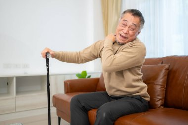 Omzu ağrıyan son sınıf öğrencisi evindeki oturma odasında bastonuyla kanepede oturuyor..