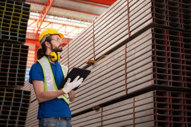 Depoda kasklı ve kasklı bir depo işçisi depodaki çeliği saymak ve incelemek için bekliyor..