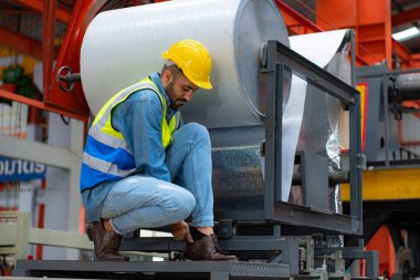 A young man works in a warehouse storing rolls of metal sheet material. Sit down break and wipe off sweat a little before continuing with work. clipart