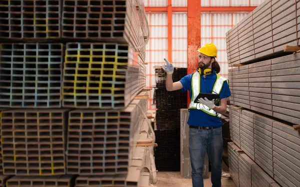 Depoda kasklı ve kasklı bir depo işçisi depodaki çeliği saymak ve incelemek için bekliyor..