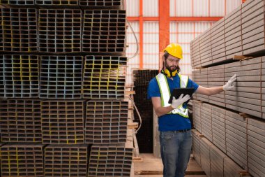 Depoda kasklı ve kasklı bir depo işçisi depodaki çeliği saymak ve incelemek için bekliyor..