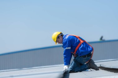 Bir teknisyen deponun çatısına güneş enerjisini fabrikalarda kullanmak üzere elektrik enerjisine dönüştürmek için güneş panelleri kuruyor..