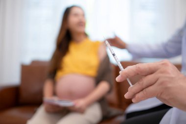 Kadın doğum uzmanı jinekolog ve aşı iğnesi ya da hamile kadın, Asyalı hamile kadın gebelik danışmanlığı için jinekolog kliniğine gitmiş..