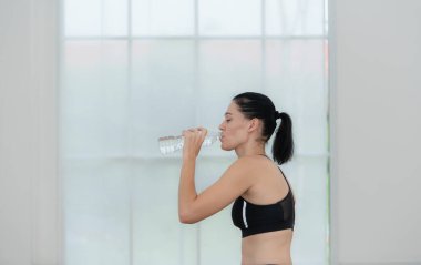 Yoga minderlerinde oturup su içen genç kadınlar. Birbirlerine bakıp gülümsüyorlar.