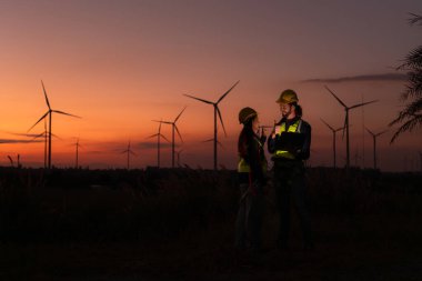 Engineers working on wind turbines farm at sunset, Wind turbines are alternative energy source. clipart