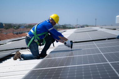 Her iki teknisyen de güneş enerjisini fabrikalarda kullanılmak üzere elektrik enerjisine çevirmek için deponun çatısına güneş panelleri kuruyor..