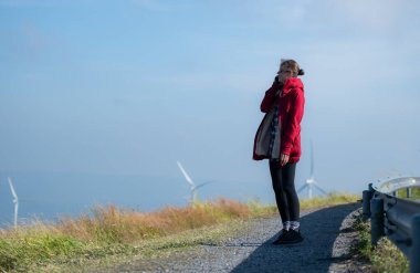Yel değirmenlerinin arka planında, kırmızı ceketli genç bir kadın kış tatilinin tadını çıkarıyor..