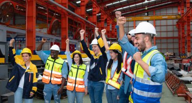 Bir grup kasklı fabrika işçisi başarıyı kutlarken kollarını kaldırdılar.