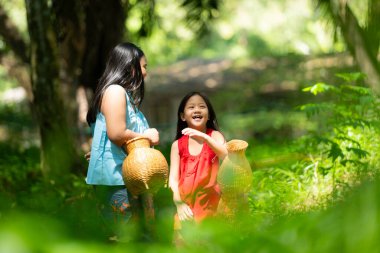 Geleneksel giyinen iki Asyalı kız yağmur ormanlarında ayakta duruyor. Büyükbabaya yakınlardaki bir gölde balık tutmasında yardım etmeden önce birlikte oynayarak eğlendiler..