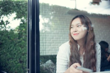 Kafede akıllı telefon kullanan Asyalı güzel bir kadının portresi.